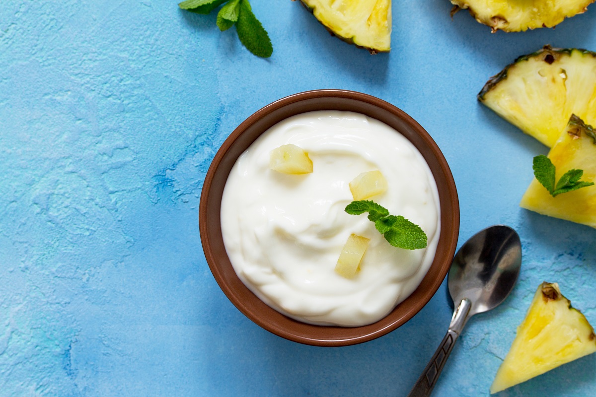 Homemade healthy breakfast. Greek yogurt in a bowl with pieces fresh pineapple on blue stone or concrete table. Copy space, top view flat lay background.